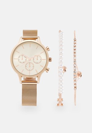 Gouden meshbandhorloge met een lichte wijzerplaat, drie subdials en rosegouden accenten. Inclusief een parelarmband en een armband met kristallen.