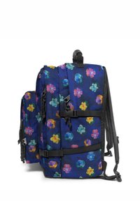 Ryggsäck med ett blått mönstrat tyg som har färgglada blommönster, justerbara remmar och sidofickor med metallaccenter.