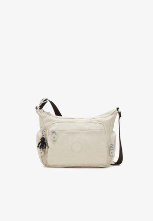 Sac bandoulière beige avec plusieurs poches zippées, un patch logo rond et un petit porte-clés singe noir attaché à la fermeture éclair avant.