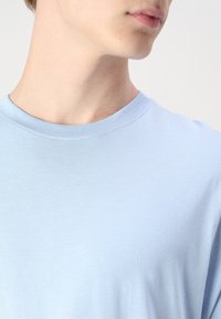 Light blue cotton t-shirt with a crew neck. Fabric is smooth with a slight stretch, featuring a simple, solid color without patterns.