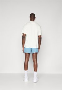 Kremkrāsas īsām piedurknēm T-krekls un zili šorti ar saplīsis apakšmalu, apvienoti ar baltām kedām un potīšu zeķēm. Minimalistisks dizains.