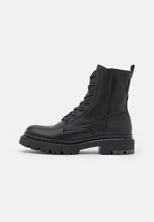Botte de combat noire à lacets avec semelle épaisse crantée, tige montant à la cheville, bout rond et languette à l'arrière, vue de profil.