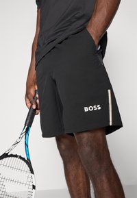 Svarta träningsshorts i lätt material, med en vit "BOSS"-logotyp, sidofickor och en tunn vertikal randdesign.