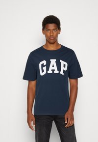 Navy blue cotton t-shirt featuring the word "GAP" in large white letters. Crew neck, short sleeves, and a standard fit.