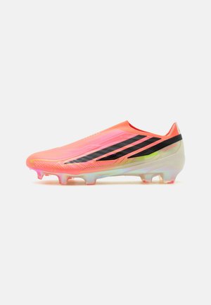 Chaussure de football rose fluo avec des rayures noires, semelle irisée et crampons moulés, conçue pour jouer sur terrain ferme.