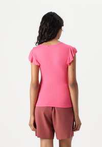 Top de manga corta acanalado en un brillante tono de rosa con mangas con volantes; combinado con pantalones cortos marrones. Diseño sencillo con un escote redondo en la parte posterior.
