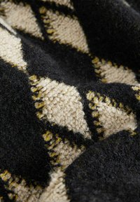 Couverture tissée en noir, crème et jaune, avec une surface en peluche texturée, présentant un motif en losange et des bords frangés.