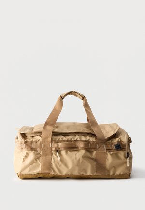 Sac de sport rectangulaire beige avec poignées doubles, plusieurs compartiments zippés et fond renforcé sur un fond clair uni.