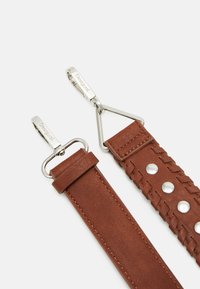 Cinturino in pelle marrone caratterizzato da un design intrecciato con bottoni a pressione in argento e hardware metallico con nome del marchio inciso.