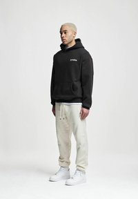 Mustra mustriga mustre ja valge logoga must kapuutsiga särk, kokku sobitatud heleda beeži treeningpüksiga ja valgete tossudega. Sile kangas, mugav lõige.