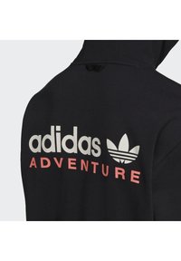 Juodas gobtuvas su medvilnės mišiniu. Yra baltas "adidas" logotipas ir žodis "ADVENTURE" rožine spalva. Įtrauktas pagalbinis Adidas trefoil akcentas.