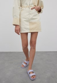Denim minirok in crème en beige kleurblokontwerp, met een tailleband en voorzakken. Gepaard met lichtpaarse sandalen.