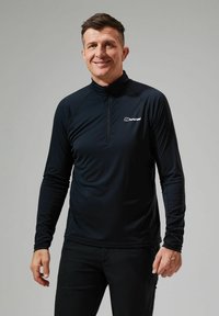 Langsleeve, strakke zwarte performance top met een kwart-rits kraag en logo op de borst. Gemaakt van lichtgewicht, gladde stof.