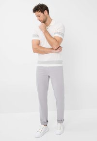 Polo in crema con strisce orizzontali grigie, abbinato a pantaloni grigio chiaro e sneakers bianche. Design semplice, tessuto morbido e vestibilità su misura.