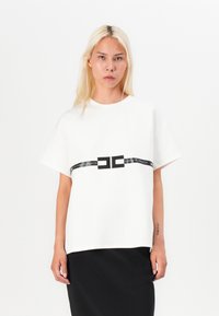 White short-sleeve t-shirt made of soft fabric, featuring a black logo band across the chest, paired with a black skirt.