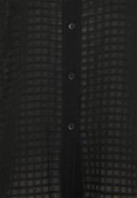 Chemise noire à carreaux transparente avec un devant boutonné et des boutons noirs. Tissu léger avec une texture en grille.