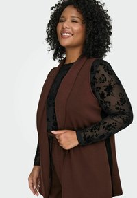 Hnědý bezrukávový kardigan přes černý průhledný dlouhý rukáv s květinovým vzorem. Texturovaná látka s otevřeným předním designem.