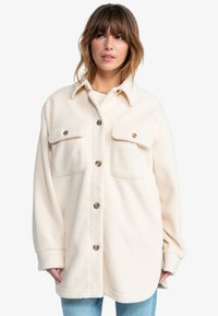 Kremfarget fleece skjortejakke med krage, to brystlommer og brune knapper. Har en avslappet passform og strukturert stoff.