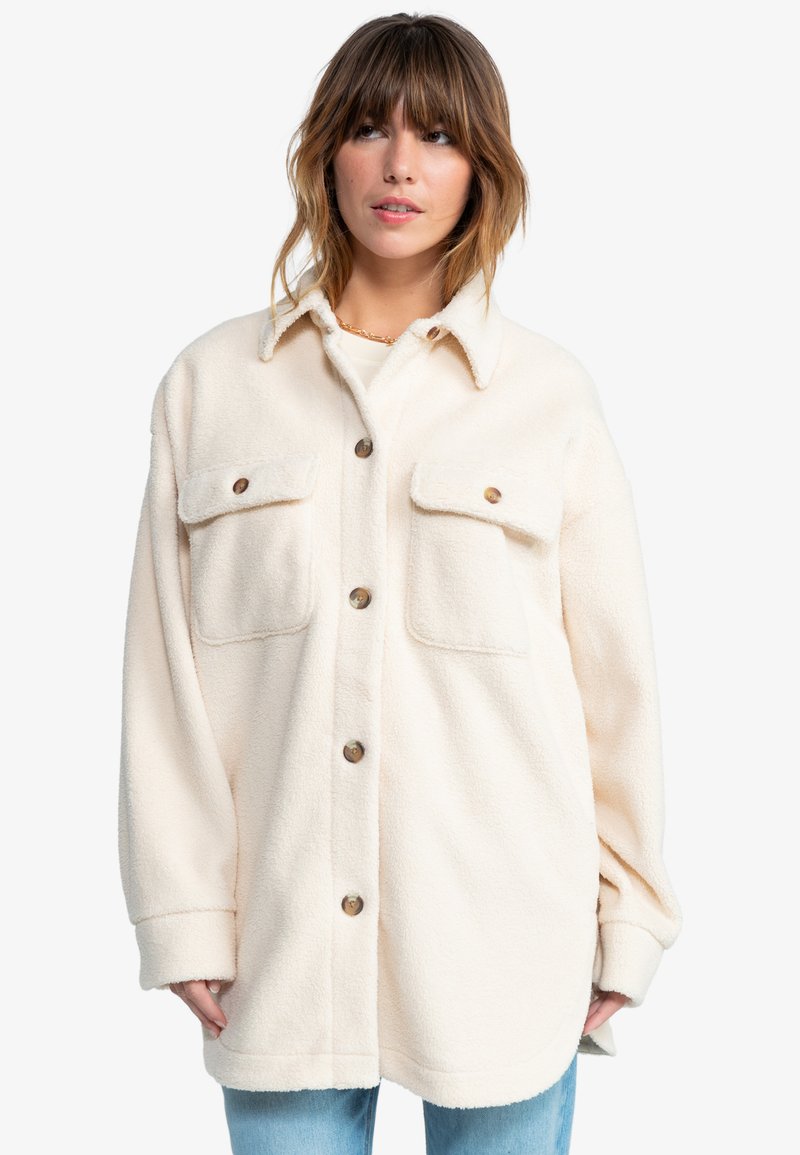 Kremfarget fleece skjortejakke med krage, to brystlommer og brune knapper. Har en avslappet passform og strukturert stoff.