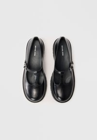Pair of black leather Mary Jane shoes with T-strap and silver buckle, branded "Michael Kors," on white background.