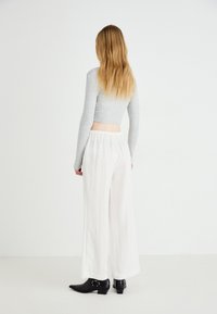 Gray long-sleeve crop top, flowy white wide-leg pants with an elastic waistband, and black ankle boots with decorative buckles.