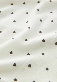 Bílá látka s hladkou texturou, zdobená malými rovnoměrně rozmístěnými hnědými vzory ve tvaru srdcí. Vzor je jemný a minimalistický.