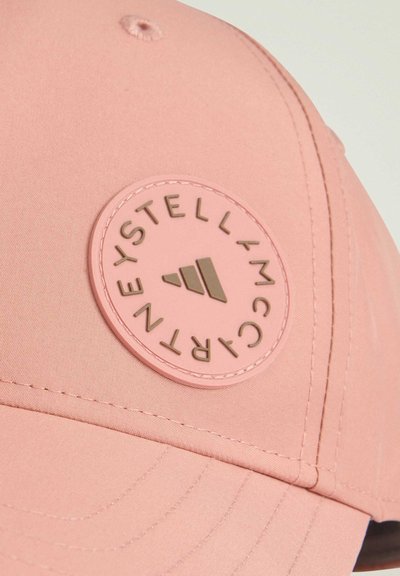 Roze kapa od glatkog materijala s okruglim, utisnutim logotipom u zlatnoj boji s bijelim tekstom. Šivanje duž vizira dodaje detalje.