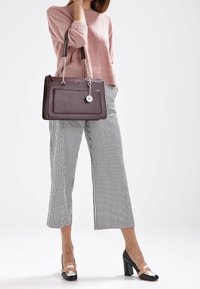 Světlá růžová pletená svetr, černobílé pruhované zkrácené kalhoty, hnědá kabelka se stříbrnými kovovými prvky a visačkou, černé podpatky s růžovými akcenty.