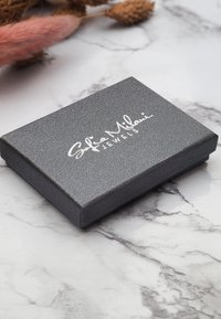 Graue, strukturierte Geschenkbox mit der eingeprägten Aufschrift "Sofia Milani Jewels" in Silber. Geschlossen, mit abgerundeten Kanten.