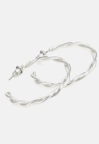Boucles d'oreilles en argent torsadé avec une finition métallique brillante et un système de fermeture à tige. Présente une texture lisse et arrondie.