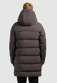 Lang, fyldig, mørkegrå parka med hætte. Har vandret quiltede sektioner og en sidelommer med lynlås. Glat, mat tekstur.