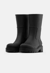 Par črnih mat gumijastih škornjev do sredine tele s debelimi zareznimi podplati na enobarvni svetlo sivi ozadju.