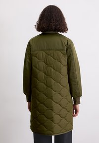 Olivengroene gewatteerde jas met een getextureerd golfpatroon, voorzien van een kraag en lange mouwen, die boven de knie eindigt.