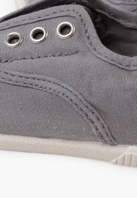 Basket en toile grise vue de côté avec œillets métalliques, double couture et semelle en caoutchouc blanche visible sur fond blanc.