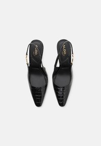Črne slingback pete z ostrim nosom, krokodilsko teksturo in zlatimi okraski. Gladek črn notranji del in minimalističen dizajn.