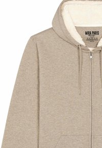 Felpa con zip beige con un morbido rivestimento interno texturizzato e tasche frontali. Presenta stringhe regolabili e un'etichetta sul colletto.