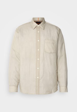 Ανοιχτό μπεζ μακρυμάνικη μπλούζα με κουμπιά μπροστά, μία θήκη στο στήθος και μαλακό, ελαφρώς υφασμένο ύφασμα. Λεπτομέρειες στον γιακά σε αντίθεση.