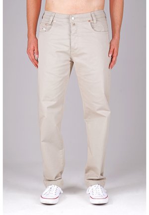 Beige Baumwollhosen mit geradem Schnitt, fünf Taschen-Design, Knopf- und Reißverschluss, und weiße Sneakers mit roten Akzenten.