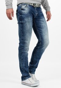 Blauwe spijkerbroeken van denim met een vervaagde was, slim-fit ontwerp en vijf zakken. Gecombineerd met witte sneakers en een grijze shirt.
