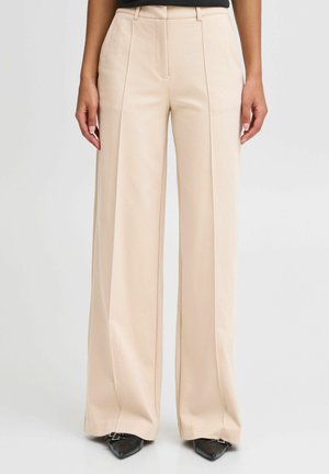 Beżowe spodnie z szerokimi nogawkami i wysokim stanem, z przednimi zakładkami, noszone z czarnymi butami na szpic i czarnym topem, pokazane od talii do stóp.