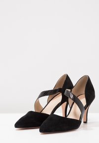Czarne zamszowe buty na wysokim obcasie z ostro zakończonym noskiem, z krzyżującym się paskiem ze skóry wężowej. Gładkie wnętrze, smukły obcas typu stiletto.