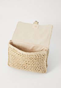 Naturlig vævet stråtaske med en beige foring, der har en knaplukning og et åbent hovedrum til opbevaring.