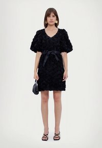 Czarna sukienka o kwiatowej fakturze, z dekoltem w kształcie litery V, z bufiastymi rękawami i paskiem w talii. Do tego czarne sandały i mała torebka.