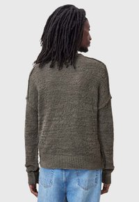 Dark green, textured knit sweater with a loose fit, ribbed cuffs and hem, and dropped shoulders, paired with light blue denim jeans.