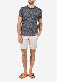Navy floral print t-shirt with short sleeves, paired with beige rolled shorts and orange sandals, featuring a flat sole and strap detail.