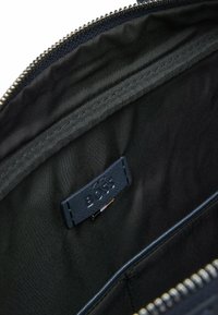 Granatowe wnętrze torby o gładkiej teksturze, z oznakowaną skórzaną metką i srebrnym suwakiem wzdłuż krawędzi.