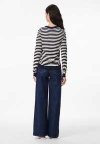 Ριγέ πουλόβερ σε ναυτικό μπλε και κρέμ, με ριμπ μανσέτες και τελείωμα; συνδυασμένο με τζιν παντελόνι ευρείας γραμμής σε σκούρο τζίν. Λείο υφή, άνετη εφαρμογή.