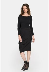 Czarna bluzka z długim rękawem zestawiona z dopasowaną czarną spódnicą do kolan. Przezroczyste czarne skarpetki do kostek oraz czarne czółenka z wydłużonym noskiem dopełniają stylizację.