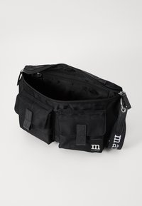 Sac à epaule en tissu noir avec fermeture éclair, dotée de deux poches avant et d'une bandoulière à logo à motif. Texture lisse avec quincaillerie fonctionnelle.