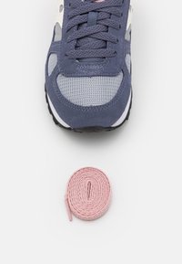 Idrettssko i marineblått, grått mesh og semsket skinn med svart såle, akkompagnert av en rosa rund snøring. Nærbilde.